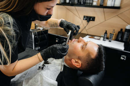 A professional stylist in a modern stylish barbershop shaves and cuts a young man's hair. Beauty salon, hair salonの写真素材