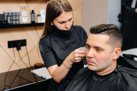 A professional stylist in a modern stylish barbershop shaves and cuts a young man's hair. Beauty salon, hair salonの写真素材