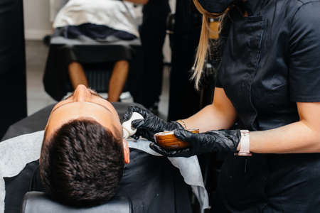 A professional stylist in a modern stylish barbershop shaves and cuts a young man's hair. Beauty salon, hair salonの写真素材