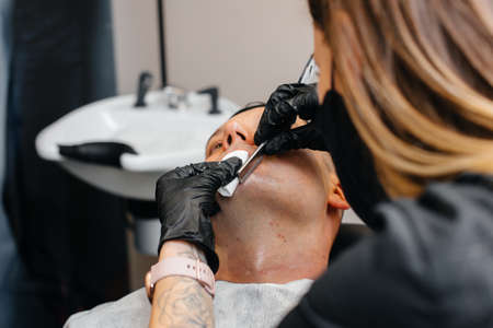 A professional stylist in a modern stylish barbershop shaves and cuts a young man's hair. Beauty salon, hair salonの写真素材
