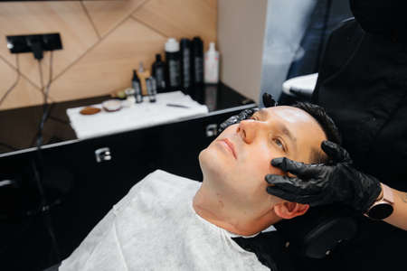 A professional stylist in a modern stylish barbershop shaves and cuts a young man's hair. Beauty salon, hair salonの写真素材