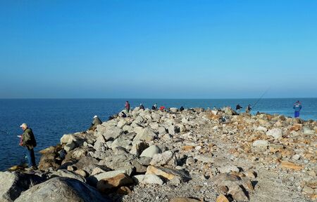 on a sunny autumn day, many anglers among the large stones of the Yeisk Spit fish in the Sea of Azovの写真素材