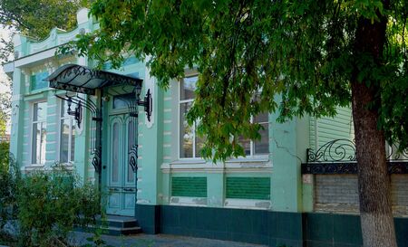 the facade of a house of old architecture of the 19th century with a door, under a carved roof, framed by trees and shrubs in the city of Yeiskの写真素材