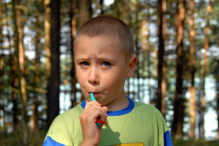Nearly 5 years young boy is brushing his teeth in forestの写真素材
