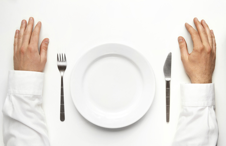 Male hands over the table waiting for dinner isolated on white. Between the two hands are plate, fork and knife. の写真素材