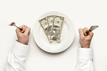 Money diet concept. Man holds fork and knife. Dollar bills and coins on plate isolated on white.