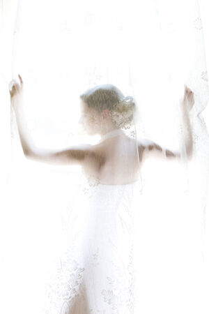 The bride standing on the window behind the curtainsの写真素材