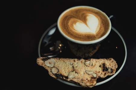 Cup of latte art on a espresso macchiato coffee with a slice of cantuccini cookieの写真素材
