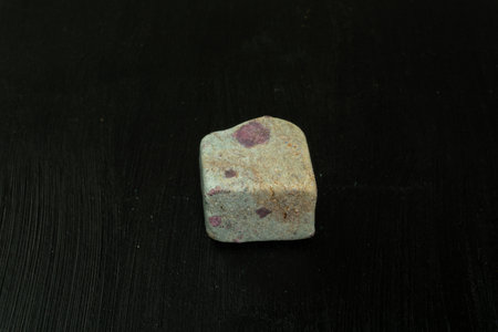 Zoisite, saualpite or ruby in the host rock. Natural mineral stone on a black background surrounded...