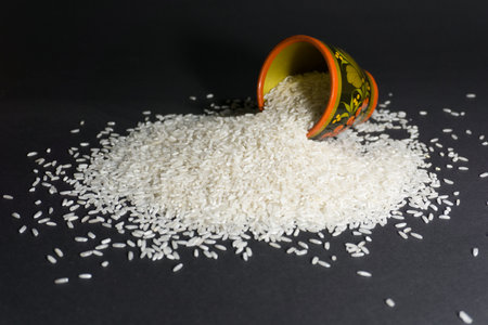 Scattered rice uncooked grains with painted wooden cup on a black backgroundの写真素材