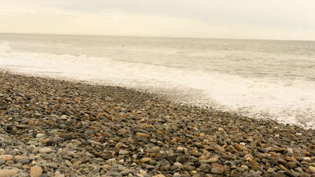 Sea stones and small pebbles with a raging sea in the background. A close-up of a rounded smooth polished pebble. Selective focus.の写真素材