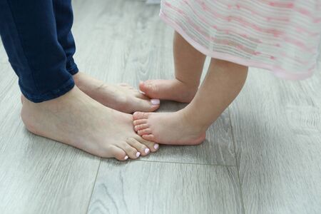Baby standing on moms feet. Close-up of the legs of mom and daughters.の写真素材