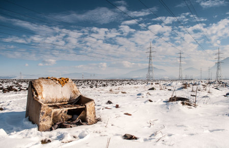An eerie scene of an abandoned armchair lying in a snow-covered field, framed by towering electrical lines against a clear sky. This image captures the stark contrast between nature and human abandonment, highlighting environmental issues and urban encroachment into rural landscapes.の写真素材