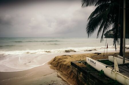 Gloomy day with rough sea on Kamala beach with view of boat moored on beach.のeditorial素材