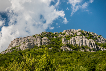 Bright blue sky with white clouds over rough mountain ridge covered with green plants on sunny dayの写真素材