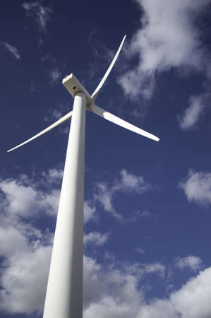 Wind turbine against a sky blue background with clouds.