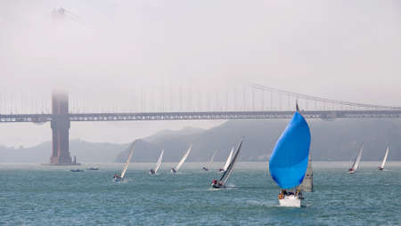 sailboat with blue spinnaker sail through the golden gate bridge shrouded in fogの写真素材