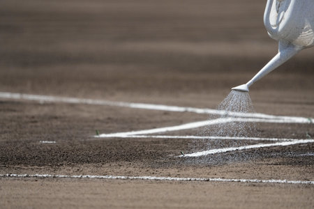 A maintenance worker sprinkles water on the batter's box with a jar on the field before a baseball game.の写真素材