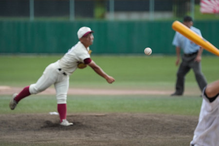 A white ball thrown by a pitcher during a baseball game and the batter's back against the pitch.の写真素材