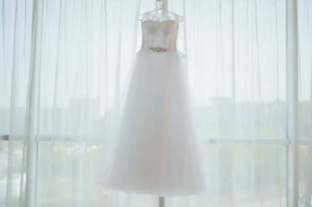 Beautiful white wedding gown hanging by windowの写真素材