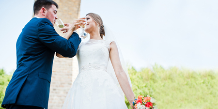fashionable and happy wedding drinking champagne from glasses under stone bridgeの写真素材