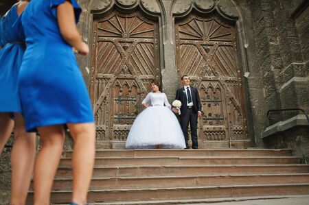 Wedding couple near old wooden door of catholic church,  legs of bridesmaidの写真素材