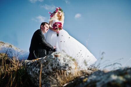 Charming bride in a wreath and elegant groom on landscapes of mountains, water and blue sky at sunny weatherの写真素材