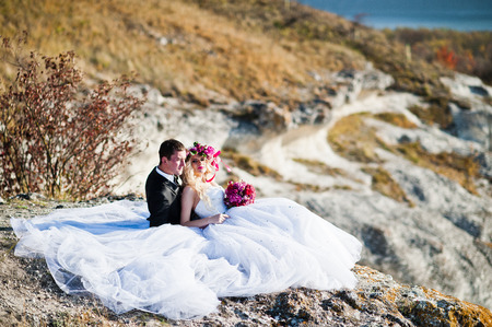 Charming bride in a wreath and elegant groom on landscapes of mountains, water and blue sky at sunny weatherの写真素材