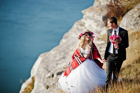 Charming bride in a wreath and elegant groom on landscapes of mountains, water and blue sky at sunny weatherの写真素材