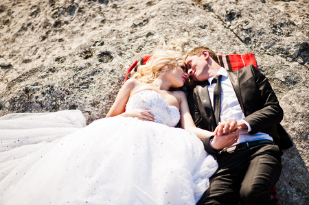 Charming bride and elegant groom on landscapes of mountains, lying on a rockの写真素材