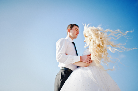 Charming bride and elegant groom on landscapes of mountains, water and blue sky at sunny weatherの写真素材