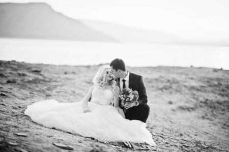 Charming bride and elegant groom on landscapes of mountains and suset at lakeの写真素材