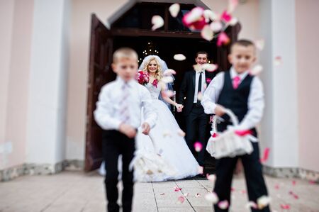 Wedding couple out from church registration, children strew petals of roses