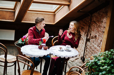 Young beautiful stylish couple in a red dress in love story at the vintage cafe with big windows at the roofの写真素材