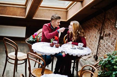 Young beautiful stylish couple in a red dress in love story at the vintage cafe with big windows at the roofの写真素材