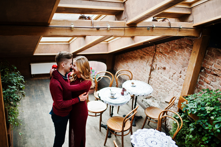 Young beautiful stylish couple in a red dress in love story at the vintage cafe with big windows at the roofの写真素材