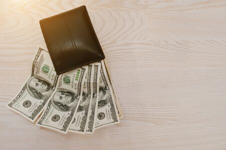Dollars in the black leather wallet on white wooden background