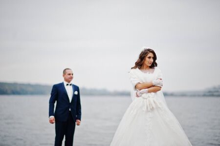 Close up wedding portrait of couple in cloudy weather on the background of the pier at the lake