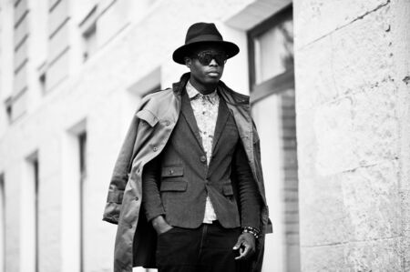 Fashion portrait of black african american man on green velvet jacket, black hat and coat cloak on his shoulders walking on streets of city background house with many windows. B&W photoの写真素材