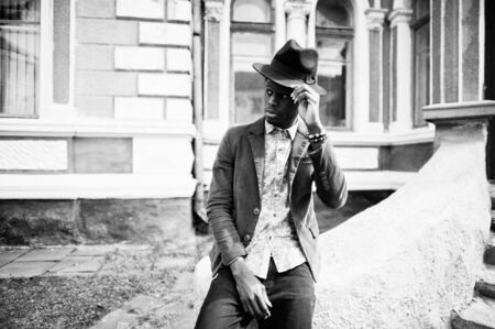 Close up fashion portrait of black african american man on green velvet jacket and black hat sit on stairs background old mansion. B&W photoの写真素材