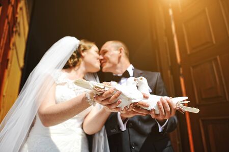 Kissing wedding couple with pigeons in they hands at sunbeamの写真素材