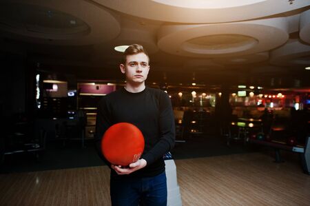 Young man holding a bowling ball standing against bowling alleys with ultraviolet light.の写真素材