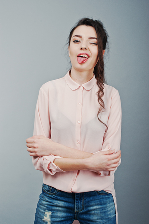 Portrait of young brunette girl showing tongue and winks, wearing in pink blouse, ripped jeans. Fashion studio shotの写真素材