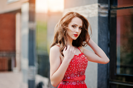 Close up portrait of fashionable girl at red evening dress posed background mirror window of modern buildingの写真素材