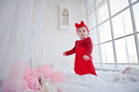 Little cute girl in red dress play on large white bedの写真素材