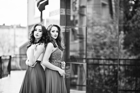 Portrait of two fashionable girls at red evening dress posed background mirror window of modern building. Black and white photoの写真素材
