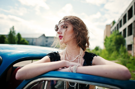 Portrait of beautiful curly fashion girl model with bright makeup in retro style leaned on a vintage...