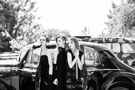 Three young girl in retro style dress near old classic vintage cars.の写真素材