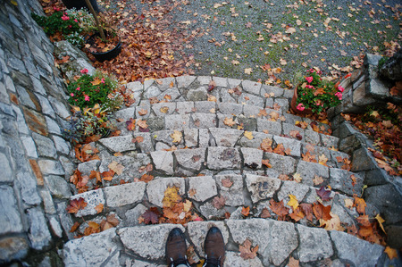 Shoes of man stay on stone stairs with autumn leaves