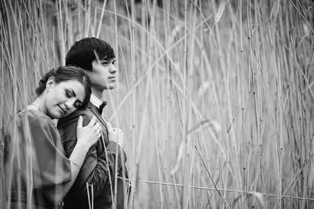 Couple hugging in love at high cane. Stylish man at velvet jacket and girl in red dress in love together. Black and white photoの写真素材